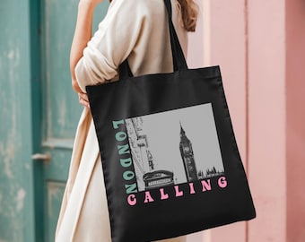 Puede incluir: Bolsa de tela negra con un gráfico blanco de Big Ben y una cabina telefónica roja. El texto "LONDON CALLING" está impreso en verde y rosa en la bolsa.
