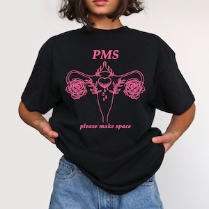 Könnte beinhalten: Schwarzes T-Shirt mit einer pinkfarbenen Grafik einer Gebärmutter mit Blumen und dem Text "PMS please make space".