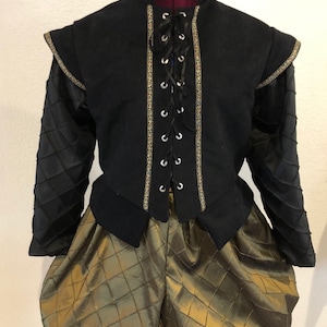 May include: A black doublet with gold trim and a lace-up front, worn over gold-colored quilted breeches.