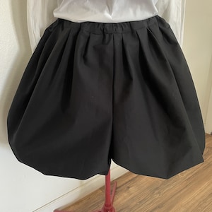 May include: Black, high-waisted, gathered shorts with a wide waistband. The shorts are made of a smooth, lightweight fabric and have a loose, flowing fit.