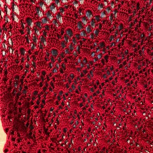 Puede incluir: Primer plano de una manta de ganchillo roja con un patrón de encaje.