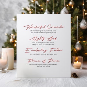 Puede incluir: Un letrero de lienzo blanco con texto rojo que dice "Wonderful Counselor", "Mighty God", "Everlasting Father" y "Prince of Peace". El texto está en una fuente de escritura a mano. El letrero está sentado sobre una superficie blanca con un cono de pino y velas en el fondo.