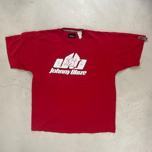May include: A red t-shirt featuring the white text "Johnny Blaze" and a graphic design. The shirt has a crew neck and short sleeves. A small label is visible on the sleeve.