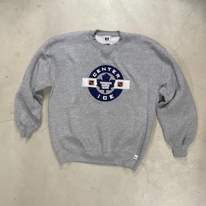 Peut inclure: Un sweat-shirt gris à col rond avec un écusson circulaire portant l'inscription "CENTER ICE" et "TORONTO MAPLE LEAFS". L'écusson est bleu avec une bande blanche et des carrés marron. Le sweat-shirt porte une étiquette Russell Athletic.