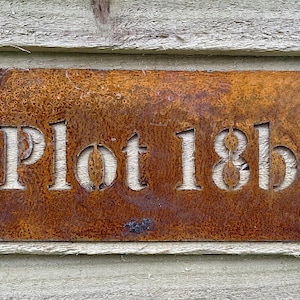 May include: A rusty metal sign with the text "Plot 18b" in white lettering.