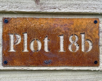 May include: A rusty metal sign with the text "Plot 18b" in white lettering.