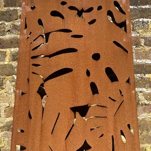 May include: A rusty metal panel with a cut-out design of abstract shapes. The panel is a reddish-brown colour and has a rough, textured surface.