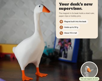 Könnte beinhalten: Eine weiße Gänsefigur mit orangefarbenem Schnabel und Füßen. Der Text auf der Produktkarte lautet: Magnet Goose, Your desk's new supervisor. The magnet in its beak holds a steel ruler, paper clips or bobby pins. Magnet built into the beak, Holds up to 50 g, About 25.4 cm tall.
