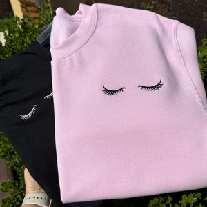 Peut inclure: Deux sweats, un noir et un rose, avec un motif brodé simple d'yeux fermés avec des cils.