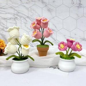 May include: Three crocheted flower arrangements in pots. The flowers are pink, white, and green. The pots are white.