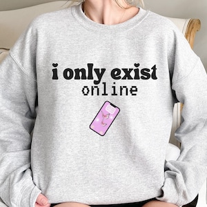 May include: Gray sweatshirt with the text "i only exist online" in black. A pink phone with a butterfly wallpaper is shown below the text.