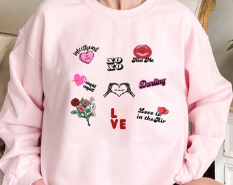 May include: Pink sweatshirt with a variety of Valentine's Day themed graphics, including hearts, lips, and the words "sweetheart", "XO", "Kiss Me", "stupid cupid", "til death", "Darling", "Love is in the Air", and "LOVE".