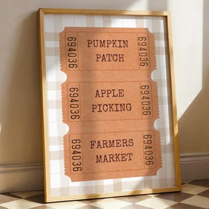 May include: A framed print featuring three vintage-style tickets. The tickets are brown with the text "Pumpkin Patch," "Apple Picking," and "Farmers Market." The background is a beige and white checkered pattern.