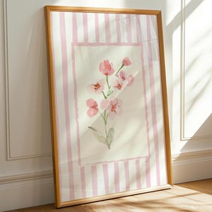 Puede incluir: Una impresión enmarcada con un fondo a rayas rosa y blanco y una pintura de acuarela de flores rosas en el centro.
