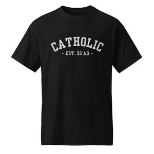 May include: Black t-shirt with the word "CATHOLIC" in white, arched lettering. Below the word is the text "- EST. 33 AD -". The shirt is a short-sleeved crew neck.