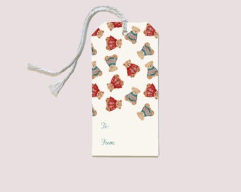 May include: A cream-coloured gift tag featuring a repeating pattern of teddy bears in red and blue sweaters. The tag has a white string and the words "To:" and "From:" are printed on it.