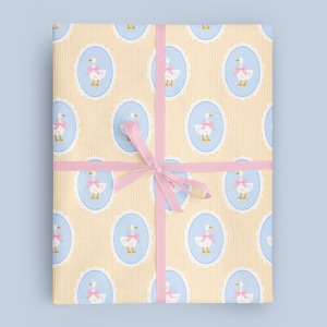 Puede incluir: Paquete de regalo envuelto en papel estampado con gansos en &oacute;valos azules con lazos rosas, sobre un fondo a rayas amarillas. El paquete est&aacute; atado con una cinta rosa.