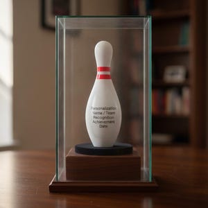 May include: A white bowling pin trophy with two red horizontal stripes near the neck, displayed inside a clear glass case on a wooden base. The pin features the printed text: Personalization, Name / Team, Recognition, Achievement, Date.