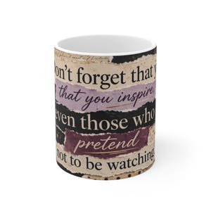 Puede incluir: Una taza de cerámica blanca con un diseño de collage de tiras de papel rasgadas en tonos beige, negro y morado. El texto impreso en la taza dice: Don't forget that you inspire, even those who pretend not to be watching.