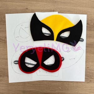 以下が含まれることがあります： フェルト製のスーパーヒーローマスク2つ。1つは赤と黒でデッドプールデザイン、もう1つは黄色と黒でウルヴァリンデザイン。マスクは黒い線のある白い紙の上に置かれています。