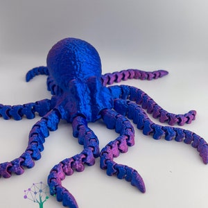 May include: A 3D printed octopus with blue and purple iridescent paint. The octopus has eight tentacles that are segmented and bendable. The octopus is posed with its tentacles spread out.