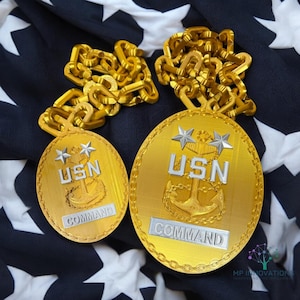 Può includere: Due medaglioni in metallo color oro con una catena. I medaglioni sono di forma ovale e presentano un'ancora argentata, due stelle e il testo "USN COMMAND".