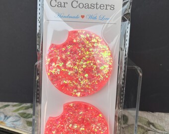 May include: Two pink car coasters with iridescent glitter. The coasters are packaged in a clear plastic bag with a white label that says "Car Coasters Handmade With Love".