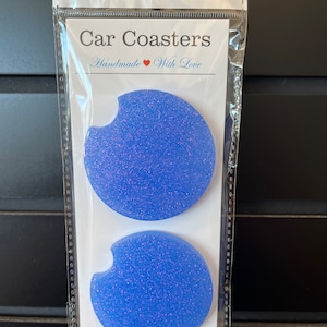 May include: Two light blue glitter car coasters with a cut-out for a cup. The coasters are packaged in a clear plastic bag with a white card that says "Car Coasters Handmade With Love".