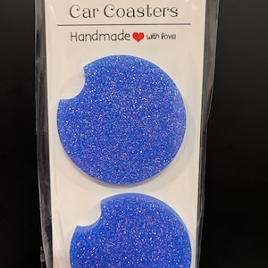 May include: Two blue glitter car coasters with a curved cutout for easy removal. The packaging reads "Car Coasters" and "Handmade with love."