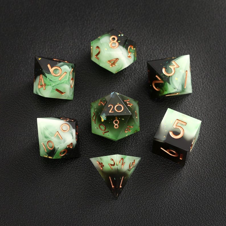 Op de afbeelding: Set van zeven polyhedrale dobbelstenen met een groen en zwart gemarmerd ontwerp. De dobbelstenen hebben koperkleurige cijfers en randen. De set bevat een D4, D6, D8, D10, D12, D20 en een percentieldobbelsteen.