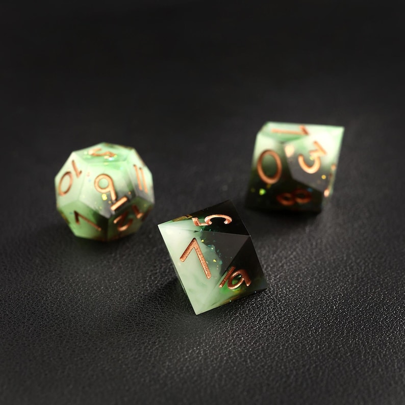 Op de afbeelding: Drie polyhedrale dobbelstenen met een groen en zwart gemarmerd ontwerp en koperkleurige nummering. De dobbelstenen zijn voor tabletop rollenspellen. E&eacute;n dobbelsteen is een 20-zijdige vorm, en de andere twee zijn verschillende polyhedrale vormen.