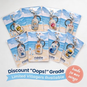 May include: A collection of keyrings, each with a different animal character inside a glass bottle. The keyrings have silver clasps and are presented on cards with a beach scene. The cards feature the text "riddle" and "Limited Villagers Available."