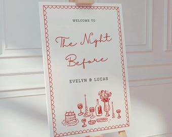 May include: A white sign with red text and illustrations announcing "Welcome to The Night Before Evelyn & Lucas". The illustration depicts a table setting with a cake, wine glasses, a bottle of wine, a vase of flowers, and a baguette.