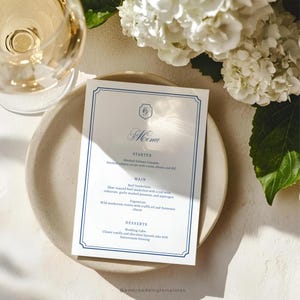 May include: A formal menu card with a blue border and elegant script. The menu lists starters, main courses, and desserts, including smoked salmon canapés and a wedding cake. The card is on a beige plate, with a glass of wine and white flowers in the background.