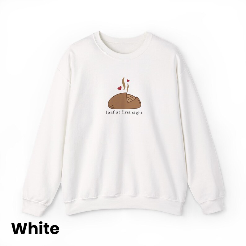 Peut inclure: Sweat-shirt blanc &agrave; col rond avec un motif de pain. Le motif comprend un pain de dessin anim&eacute; avec de la vapeur et des c&oelig;urs, et la phrase "loaf at first sight". Un style confortable et d&eacute;contract&eacute;.
