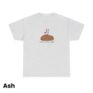 Puede incluir: Camiseta gris ceniza con un dibujo de una hogaza de pan marr&oacute;n, vapor y corazones, y el texto "loaf at first sight".