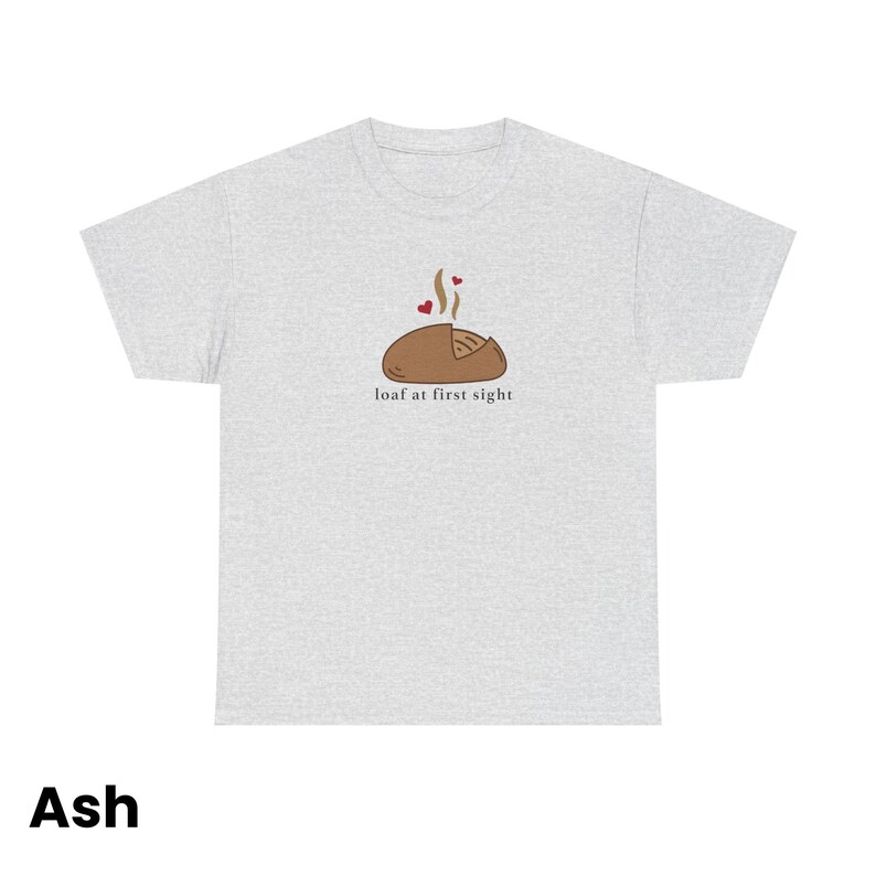 Puede incluir: Camiseta gris ceniza con un dibujo de una hogaza de pan marr&oacute;n, vapor y corazones, y el texto "loaf at first sight".