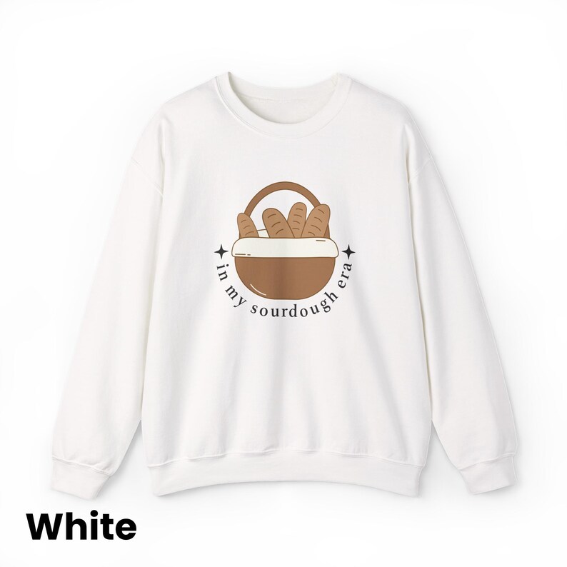 Peut inclure: Sweat-shirt blanc avec un motif de panier &agrave; pain et le texte "in my sourdough era" dans un design circulaire. Le sweat-shirt est de style col rond.