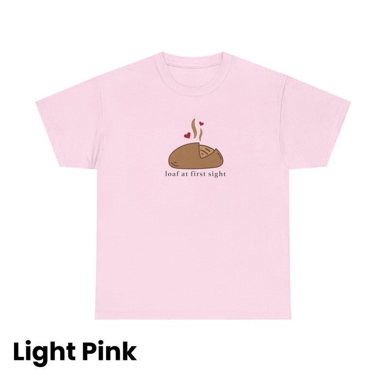 Puede incluir: Camiseta rosa claro con un gr&aacute;fico de una hogaza de pan con vapor y corazones, y el texto "loaf at first sight". La camiseta es de color rosa claro.