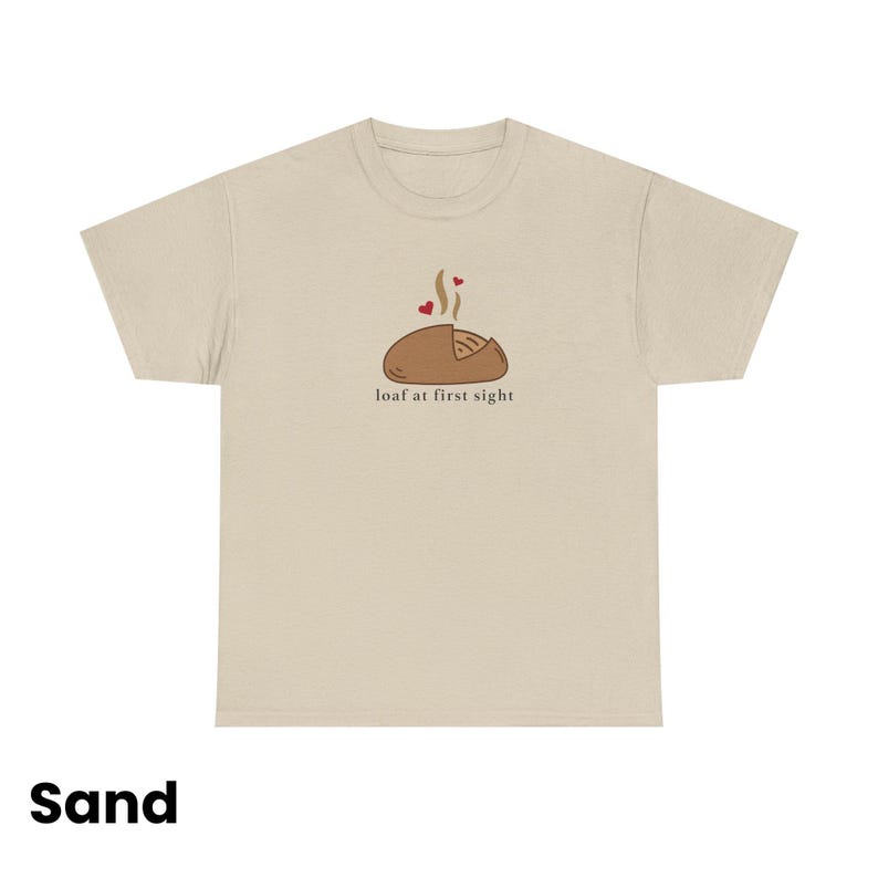 Puede incluir: Camiseta color arena con un gr&aacute;fico de una hogaza de pan con vapor y corazones, y el texto "loaf at first sight". Es una prenda de vestir informal.