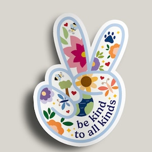 Könnte beinhalten: Ein weißer Aufkleber in Form eines Friedenszeichens, gefüllt mit farbenfrohen Illustrationen zum Thema Blumen und Natur. Das Design umfasst Blumen, Schmetterlinge, Bienen und einen Globus mit dem Text "be kind to all kinds".