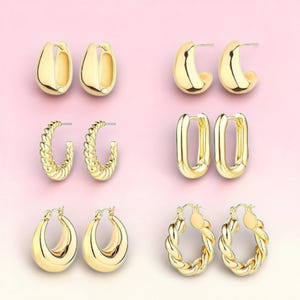 May include: A collection of gold-colored hoop earrings in various styles. The earrings include smooth, twisted, and rectangular designs. The earrings are displayed on a light pink background, showcasing their polished finish and diverse shapes.