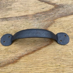 May include: Black metal cabinet handle with a rounded shape and two holes on each side.