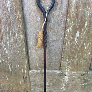 Peut inclure: Un tisonnier en métal noir avec une poignée torsadée et un crochet à l'extrémité. Le tisonnier est suspendu à un mur en bois.