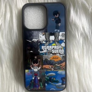 Puede incluir: Una funda de teléfono negra con un collage de imágenes. Las imágenes incluyen un personaje de dibujos animados, un cocodrilo, una nube y una mano sosteniendo un cigarrillo. El texto "AGARRAPADO EN UN SUEÑO" es visible en la funda.