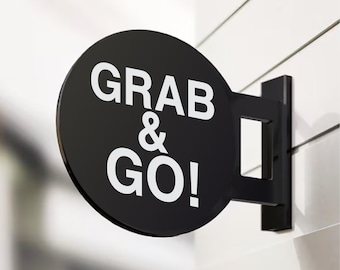 May include: Black and white sign with the text "GRAB & GO!" on a round, black background. The sign is attached to a white wall with a black metal bracket.
