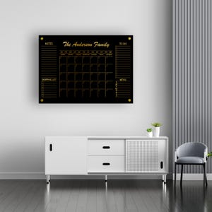 May include: Black dry-erase board with gold accents. The board has sections for notes, a calendar, a to-do list, a shopping list, and a menu. The text "The Anderson Family" is written in gold at the top of the board.