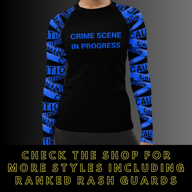 May include: Black rash guard with blue caution tape design on the sleeves. The shirt has the words "CRIME SCENE IN PROGRESS" in blue on the front. The bottom of the image has text that says "CHECK THE SHOP FOR MORE STYLES INCLUDING RANKED RASH GUARDS."