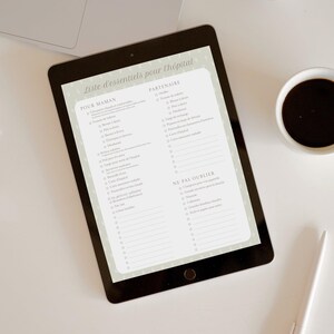 Peut inclure: Une tablette numérique affichant une liste de contrôle intitulée "Liste d'essentiels pour l'hôpital". La tablette est posée sur une surface blanche, à côté d'un ordinateur portable, d'une tasse de café et d'un stylo.