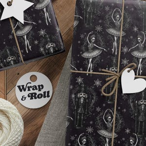 May include: Two rectangular packages wrapped in black paper featuring a white skeletal ballerina and nutcracker pattern with snowflakes, tied with brown twine and adorned with white star and heart-shaped gift tags, plus scissors and yarn.